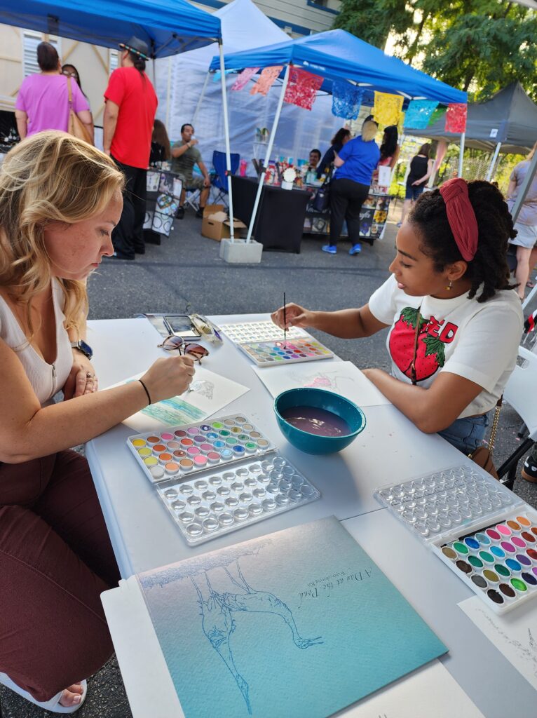 two people across table watercoloring crane drawings at Dane Arts Buy Local event